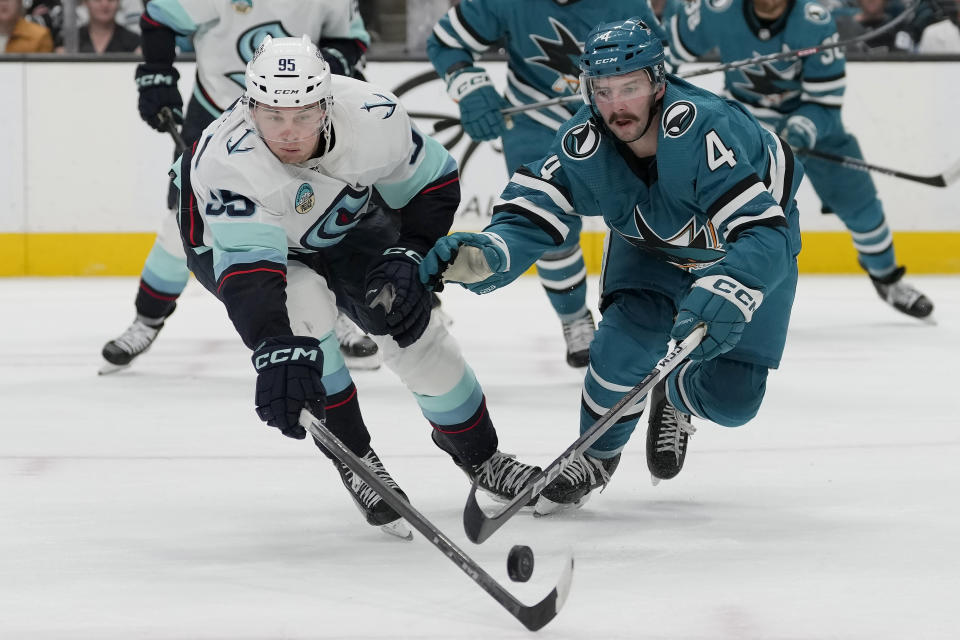 Seattle Kraken left wing Andre Burakovsky (95) reaches for the puck against San Jose Sharks defenseman Kyle Burroughs (4) during the second period of an NHL hockey game in San Jose, Calif., Monday, April 1, 2024. (AP Photo/Jeff Chiu)