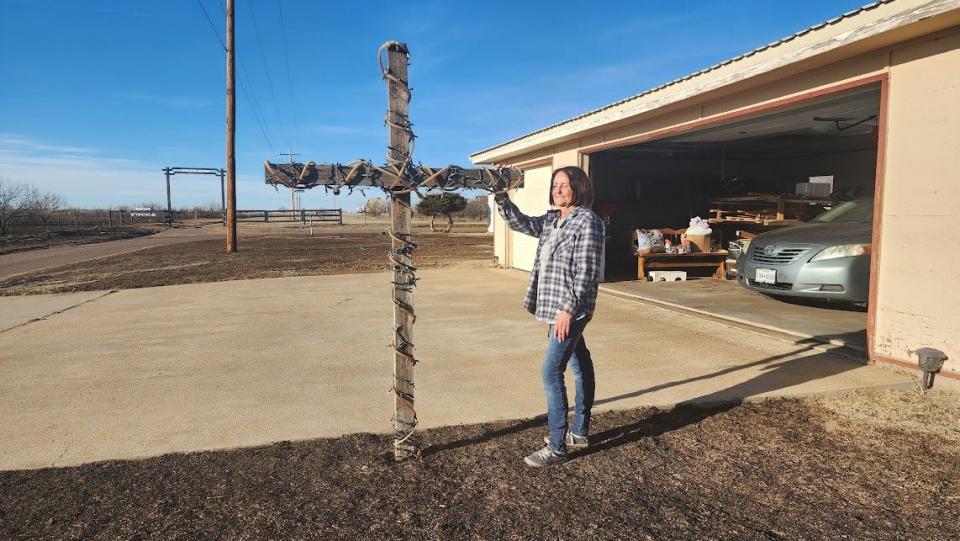 Jenny Lane stands outside of her house by her cross, both of which survived the fire which engulfed her yard in Stinnett.
