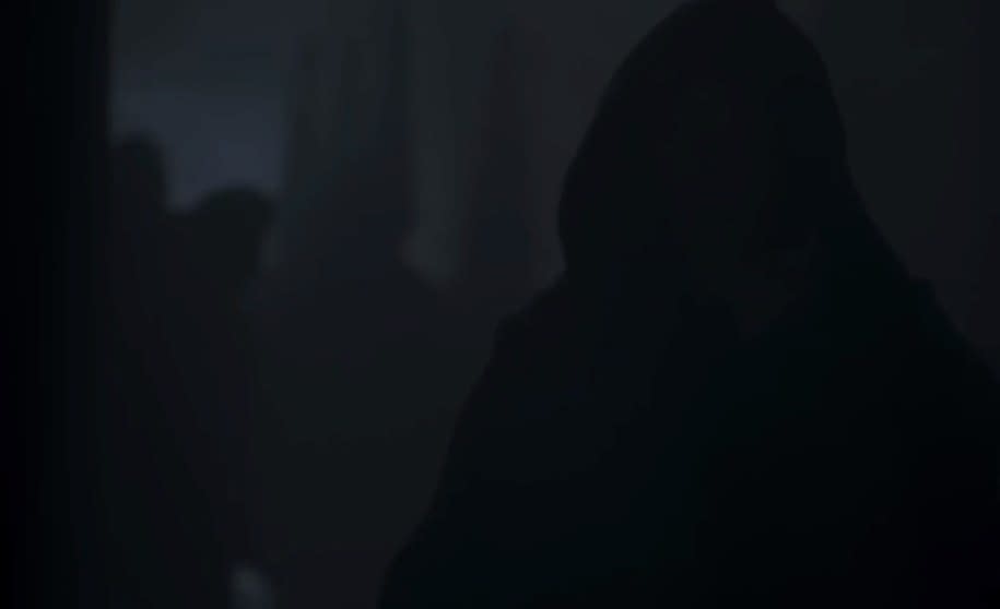 A hooded figure walks in the dark