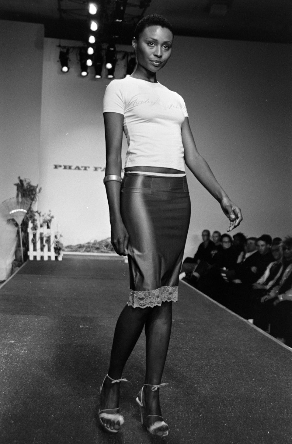 A model wears a satin skirt with lace trim and Baby Phat t-shirt with cat logo on it during Phat Farm Spring 1998 fashion show.