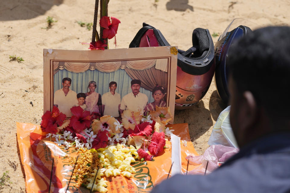 An ethnic Tamil war survivor sits by a photograph of his deceased family members during a remembrance ceremony held on a small strip of land where thousands of civilians were trapped during the last stages of the country's civil war in Mullivaikkal, Sri Lanka, Saturday, May 17, 2024. Ethnic Tamils commemorated the 15th anniversary of the bloody end to Sri Lanka's civil war, lighting lamps and offering flowers at the site where thousands of people are said to have been killed and maimed in the final stages of the fighting. (AP Photo/Eranga Jayawardena)