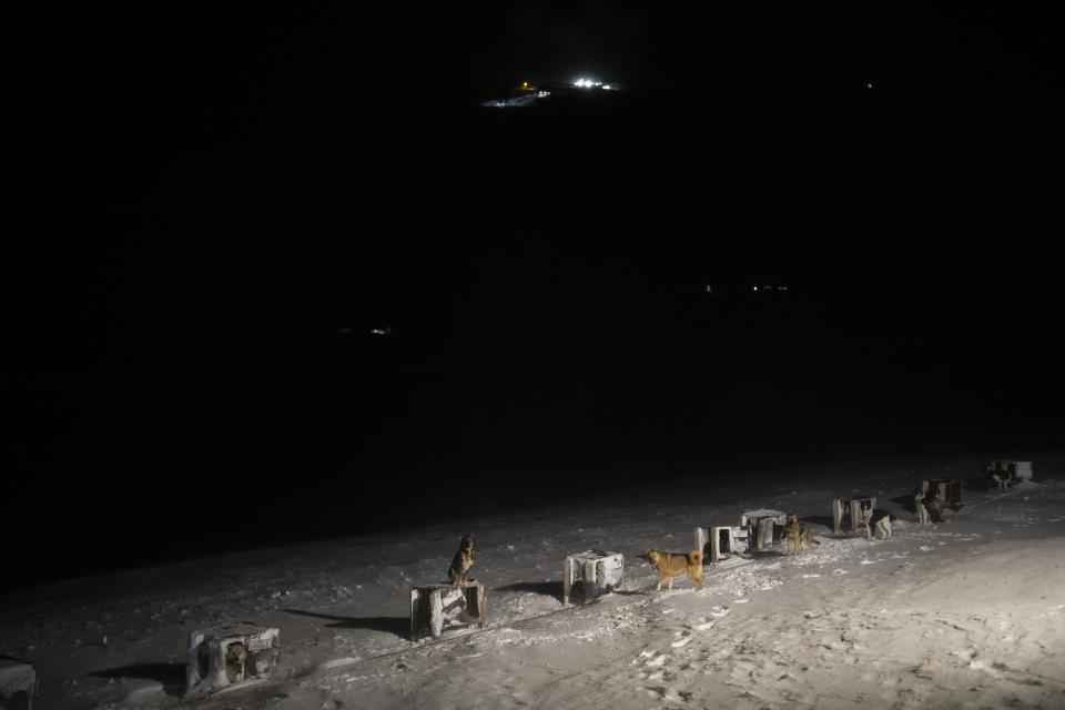 The last remaining coal mine of Longyearbyen shines on the horizon of a dog yard in Bolterdalen, Norway, Tuesday, Jan. 10, 2023. The yard is located half a dozen miles from the main village in Svalbard, a Norwegian archipelago so close to the North Pole that winter is shrouded in uninterrupted darkness. (AP Photo/Daniel Cole)