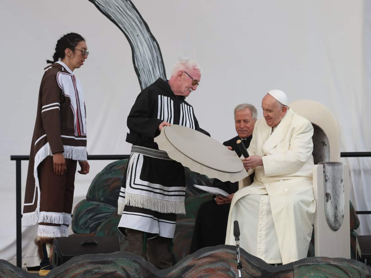 After performing a drum dance, elder Piita Irniq presents his drum to Pope Francis at the community event for the pontiff outside Nakasuk Elementary School.  (Evan Mitsui/CBC - image credit)