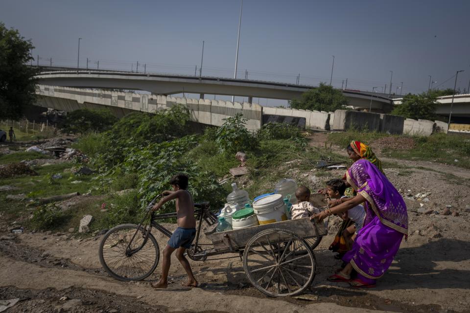 A young boy tries to steer his cycle carrier carrying drinking water down a steep slope as women try to control its speed on the way to flood plain of Yamuna River were they live in New Delhi, India, Friday, Sept. 29, 2023. (AP Photo/Altaf Qadri)