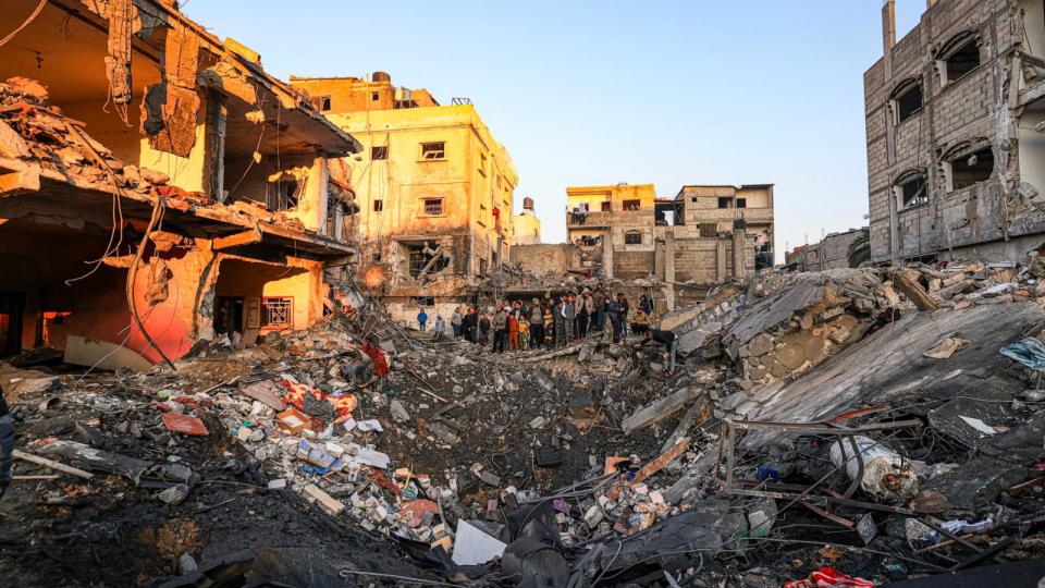 PHOTO: People stand on the edge of a crater caused by an Israeli bombardment as they inspect the destroyed building of Palestinian journalist Adel Zorob, who was killed overnight, in Rafah in the southern Gaza Strip on Dec. 19, 2023. (Mahmud Hams/AFP via Getty Images)