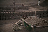 <p>Pakistani girl, Kiran Riasat, 8, who works with her mother and father, seen in the background, in a brick factory, checks on her brother, Rizwan, 1.5, laying in a hammock attached on a bed, at the site of work, in the outskirts of Islamabad, Pakistan, Feb. 18, 2014. (Photo: Muhammed Muheisen/AP) </p>