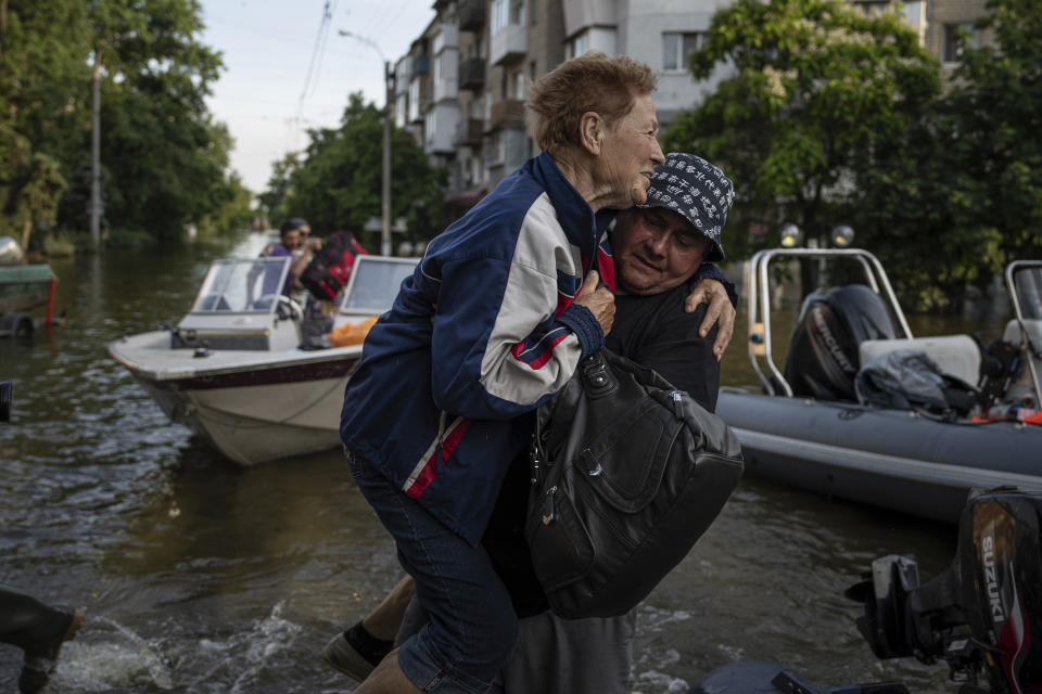 A volunteer carries a woman as she been evacuated from a flooded neighborhood of the left bank Dnipro river, in Kherson, Ukraine, Friday, June 9, 2023. In Ukraine, the governor of the Kherson region, Oleksandr Prokudin, said Friday that water levels had decreased by about 20 centimeters (8 inches) overnight on the western bank of the Dnieper, which was inundated starting Tuesday after the breach of the Nova Kakhovka dam upstream. (AP Photo/Evgeniy Maloletka)