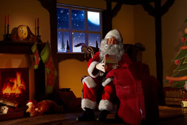 Santa holding a bag full ofchristmas gifts. He is sitting in his animated grotto. Horizontal image.