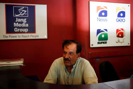 An attendant sits in front of logos at a reception desk at the Geo News television channel office in Karachi, Pakistan April 11, 2018. Picture taken April 11, 2018. REUTERS/Akhtar Soomro