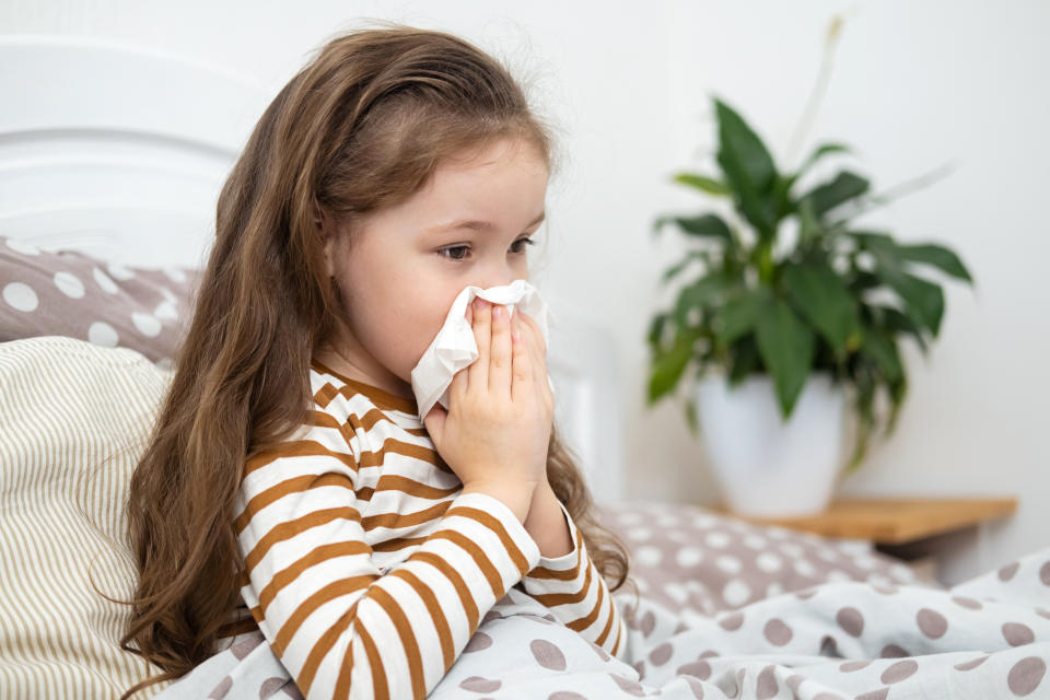 A young girl lying in bed coughs or sneezes in to a tissue. (Photo via Getty Images)