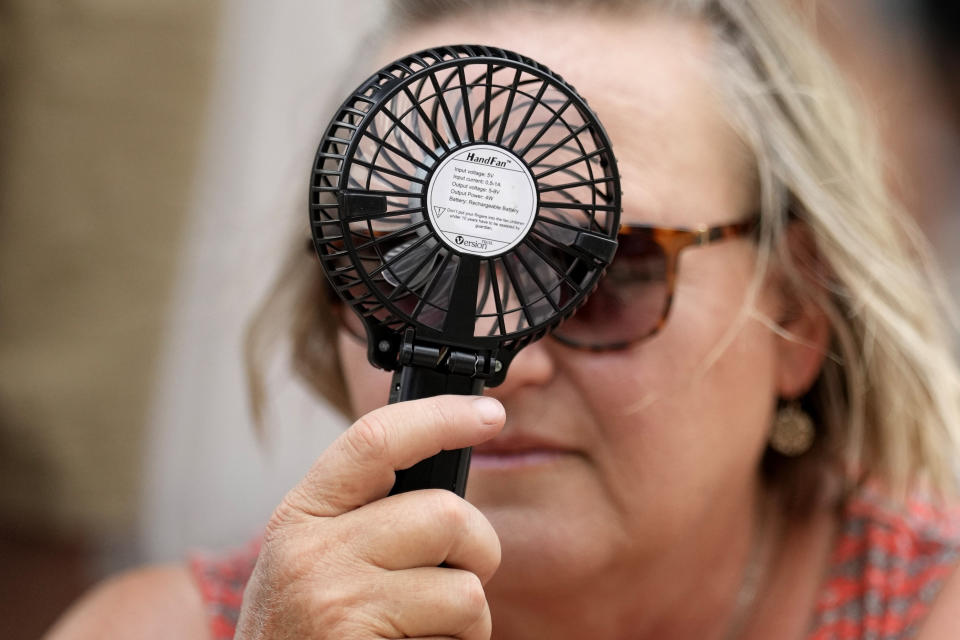 A Houston Astros fan uses a hand fan to keep cool while waiting to enter Minute Maid Park for baseball game against the Cincinnati Reds Saturday, June 17, 2023, in Houston. (AP Photo/David J. Phillip)