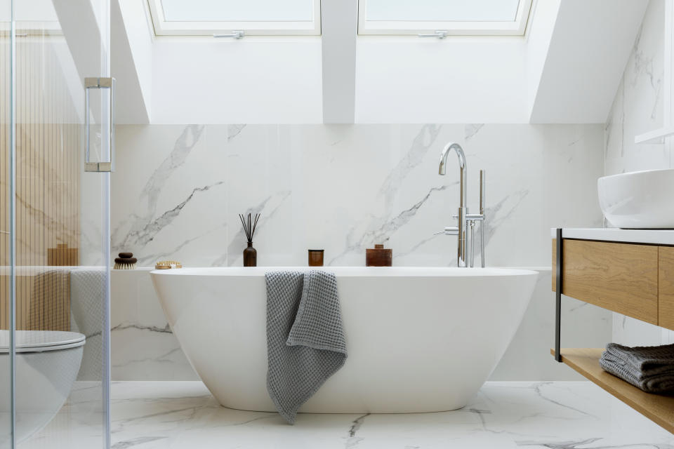 Stylish bathroom interior design with marble panels. Bathtub, towels and other personal bathroom accessories. Modern glamour interior concept. Roof window. Template.