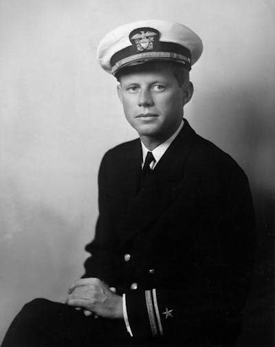 A white man is wearing a military uniform and has his hands in his lap as he poses for a photograph.