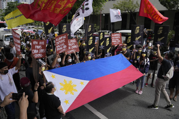 FILE - Protesters shout slogans as they hold a Philippine flag during a rally in front of the Chinese Consulate in Makati city, Philippines, on July 12, 2021. Chinese coast guard ships blocked and used water cannons on two Philippine supply boats heading to a disputed shoal occupied by Filipino marines in the South China Sea, provoking an angry protest against China and a warning from the Philippine government that its vessels are covered under a mutual defense treaty with the U.S., Manila’s top diplomat said Thursday, Nov. 18, 2021. (AP Photo/Aaron Favila, File)