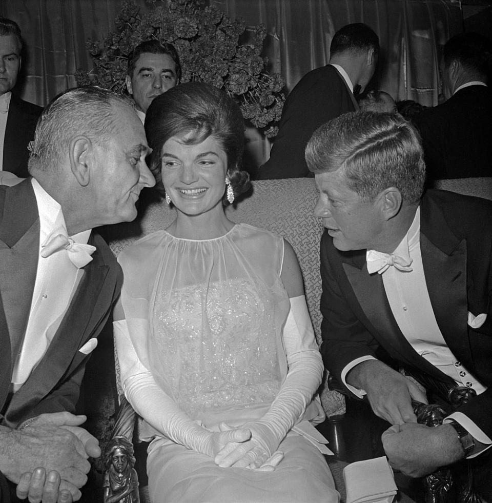 <p>While seated in the wings of the DC Armory, Vice President Lyndon B. Johnson speaks with the First Lady and President. Jacqueline Kennedy stunned in a white chiffon and sequin evening gown designed by Oleg Cassini. </p>