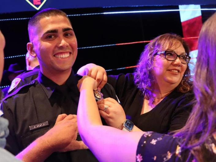 Ángel Torres (Fresno Police Department) smiles while his mother, Sylvia Torres, pins his badge on his uniform during his June 30, 2023 graduation from the State Center Police Academy at CrossCity Church.