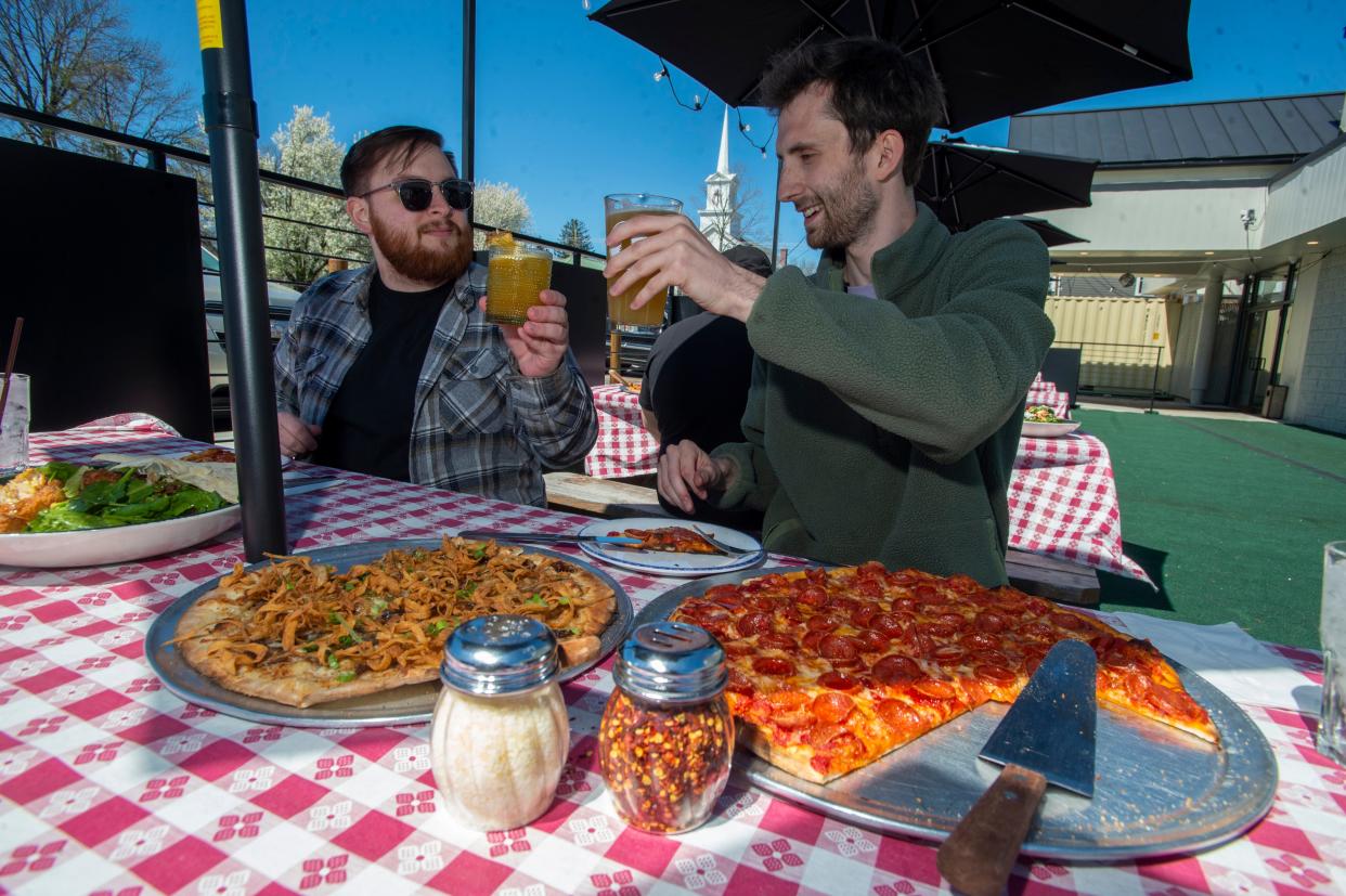 Ryan Beck, left, and Tucker Jones, both marketing team members at Rail Trail Flatbread Co., enjoy food and drink on the patio of the restaurant's Milford location, April 25, 2024.