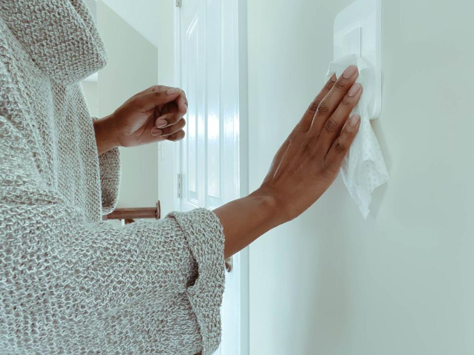 woman cleans dimmer switch using disinfectant wipe
