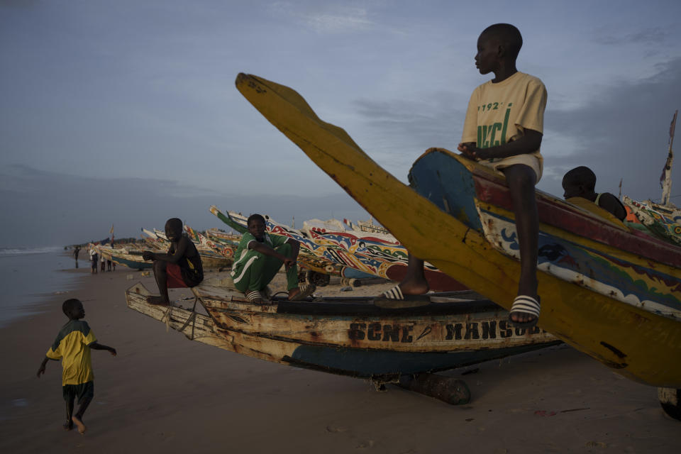 Boys sit atop pirogues, Senegalese boats used by fishermen and migrants, on the beach in Fass Boye, Senegal, Tuesday, Aug. 29, 2023. (AP Photo/Felipe Dana)