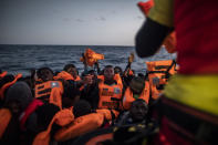 14-year old Bamba Bourahima from Ivory Coast, centre, waits to receive a life vest as rescuer Alberto Agrelo distributes them to all the migrants aboard an overcrowded rubber boat after being rescued by the Spanish NGO Open Arms rescue vessel in the Mediterranean Sea, international waters, at 80 miles off the Libyan coast, Saturday Feb. 13, 2021. Various African migrants drifting in the Mediterranean Sea after fleeing Libya on unseaworthy boats have been rescued. In recent days, the Libyans had already thwarted eight rescue attempts by the Open Arms, a Spanish NGO vessel, harassing and threatening its crew in international waters. (AP Photo/Bruno Thevenin)