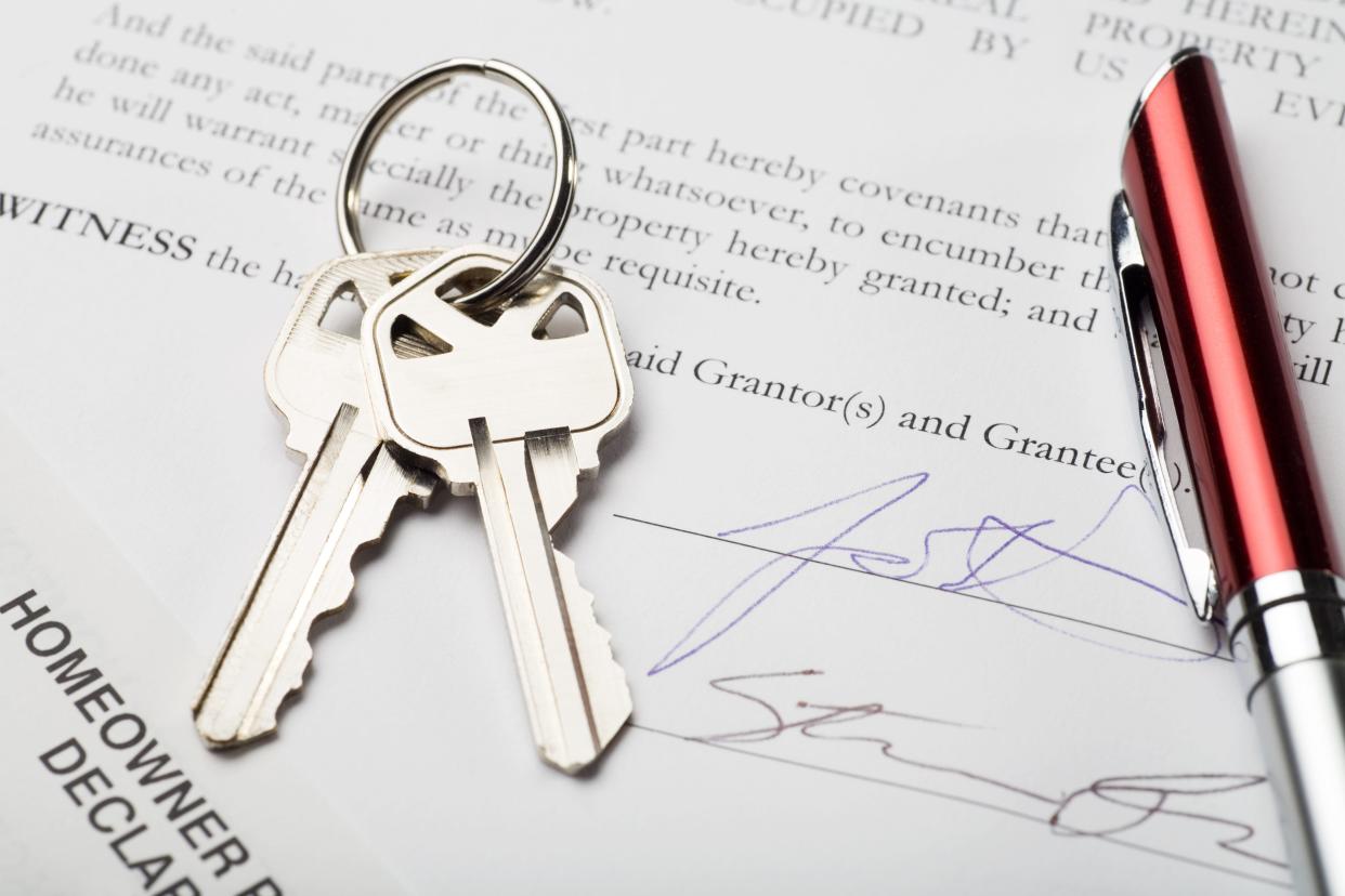 A pair of silver house keys and a red pen sit on top of a signed house deed.