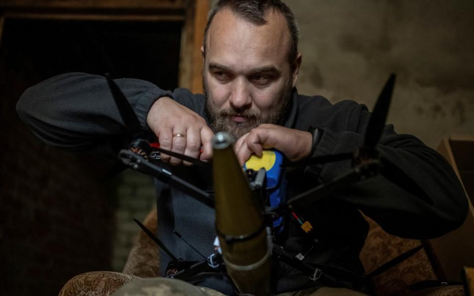 A Ukrainian soldier attaches a shell to a first person view (FPV) drone at his front line position