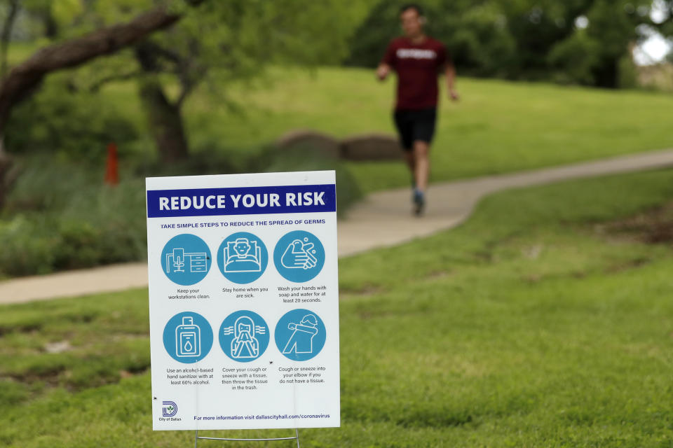 A jogger runs along a trail past a City of Dallas health sign advising people on how to reduce the risk of spreading germs amid concerns of spreading the COVID-19 virus in Dallas, Tuesday, March 31, 2020. (AP Photo/Tony Gutierrez)