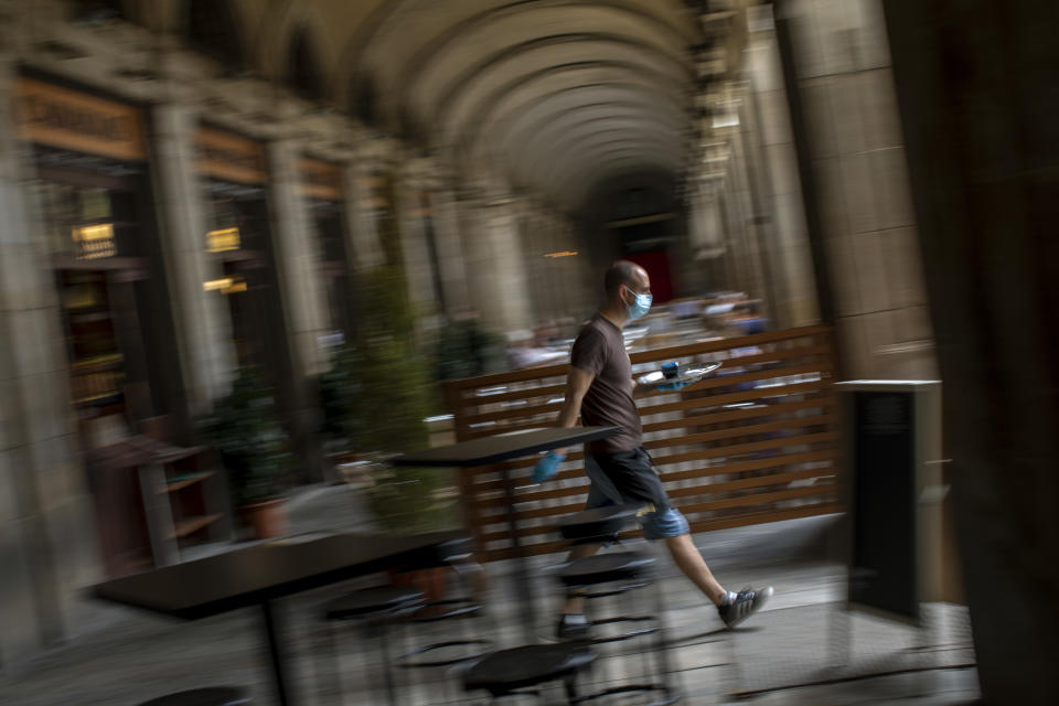 In this Monday, June 1, 2020 photo, a waiter attends local customers in a terrace bar in Barcelona. Spain is waiting until July to reopen its border for foreign tourists. In the meantime, authorities are encouraging Spaniards to vacation inside at home. (AP Photo/Emilio Morenatti)