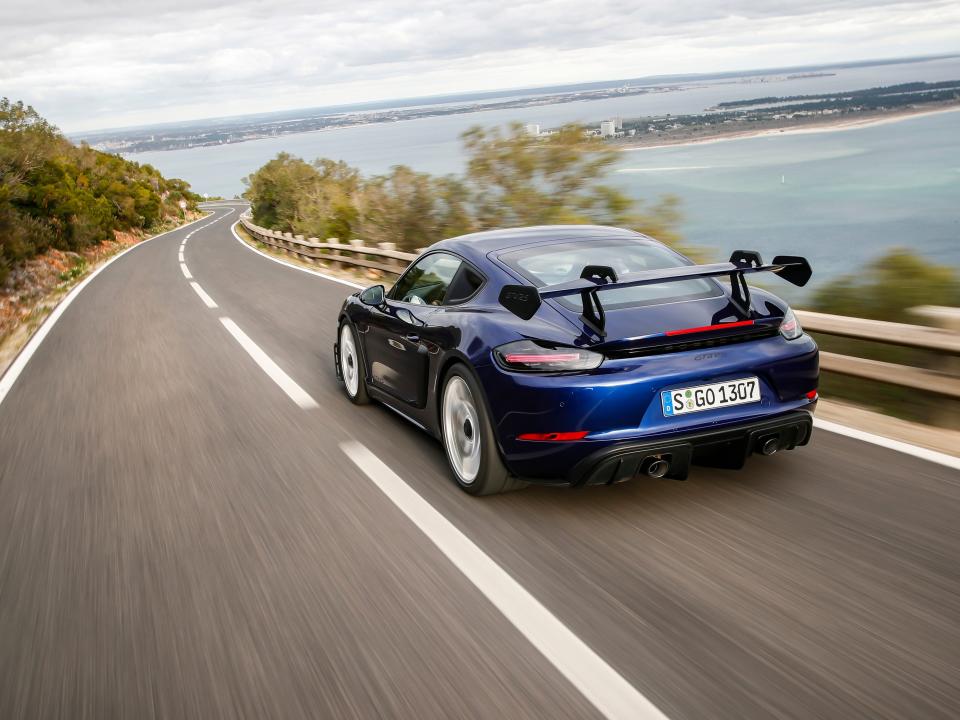 A blue Porsche drives down the road in a coastal area.