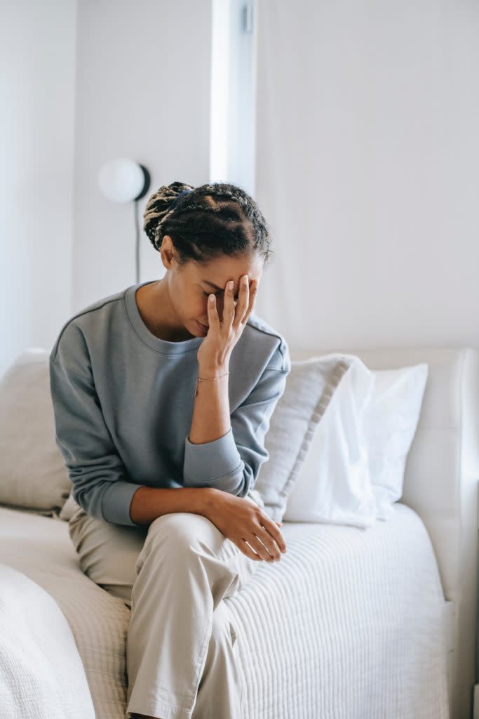 Embarrassed woman covering her face as she sits on the edge of a bed