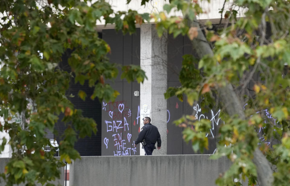 A police officer walks past a wall left with graffiti by pro-Palestinian protesters at the California State University, Los Angeles, Thursday, June 13, 2024. A takeover of a building at California State University, Los Angeles, by demonstrators protesting Israel's war against Hamas in Gaza ended early Thursday, leaving the facility trashed and covered with graffiti. (AP Photo/Damian Dovarganes)