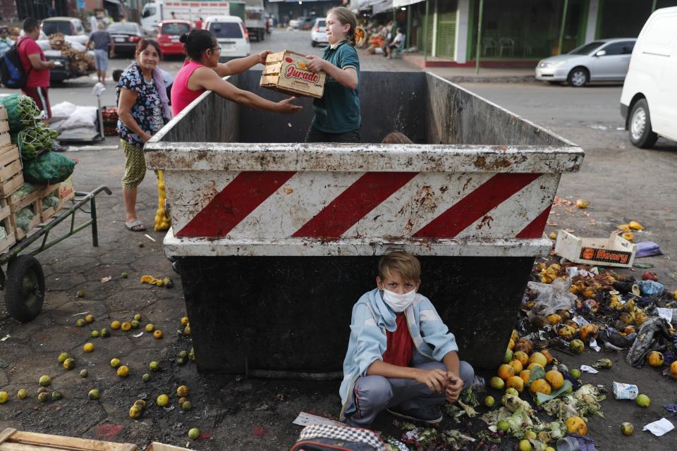 Fabian Ramirez, 11, and members of his family scavenge a trash container for discarded vegetables at the "Mercado de Abasto," a market for vendors, during the fourth week of quarantine to contain the spread of the new coronavirus in Asuncion, Paraguay, Thursday, April 2, 2020. (AP Photo/Jorge Saenz)
