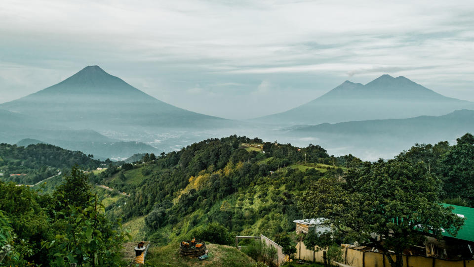 Two distant volcanoes behind a misty landscape with scattered greenery and a clear foreground