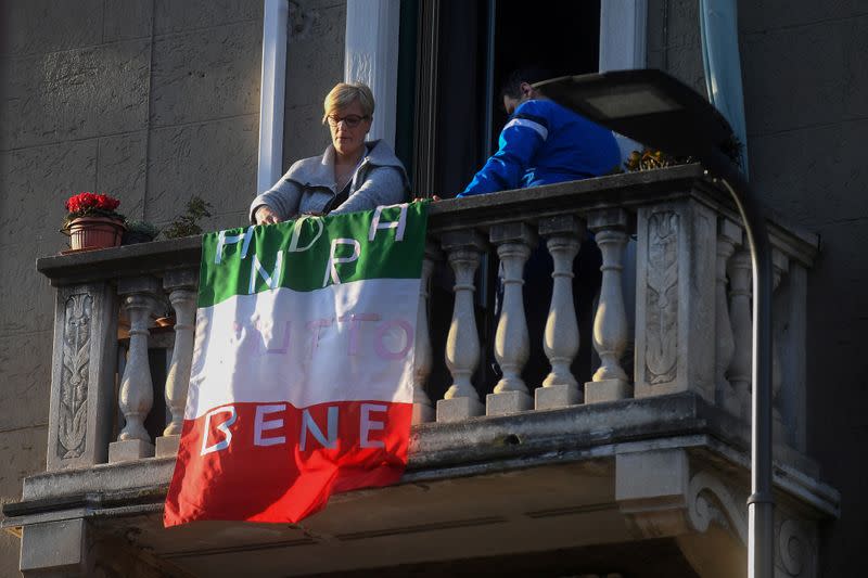 A woman places an Italian flag that reads "everything will be alright" on her apartment balcony as part of a flashmob organised to raise morale during Italy's coronavirus crisis, in Milan