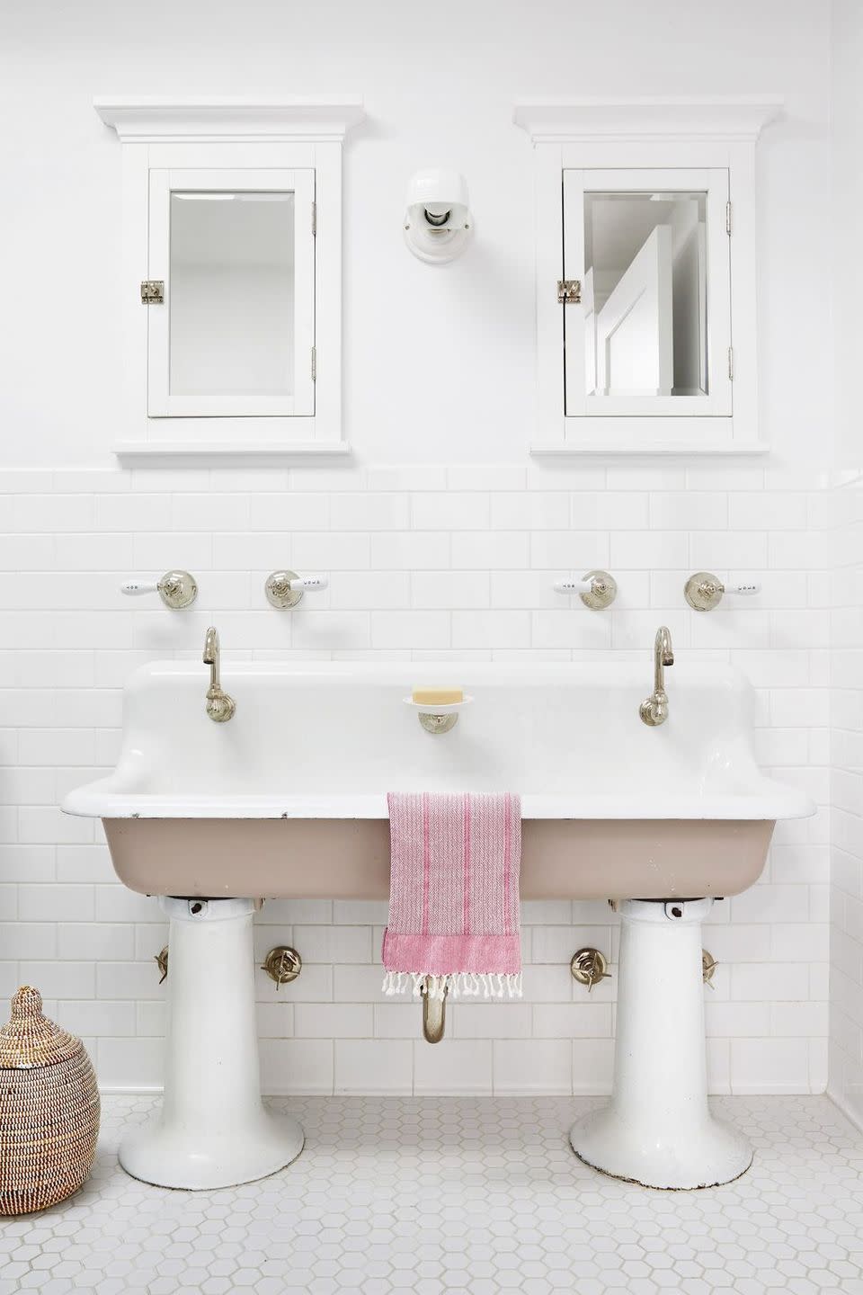 all white bathroom with hex tile floor, subway tile walls, antique pedestal style double sink, two matching medicine cabinets