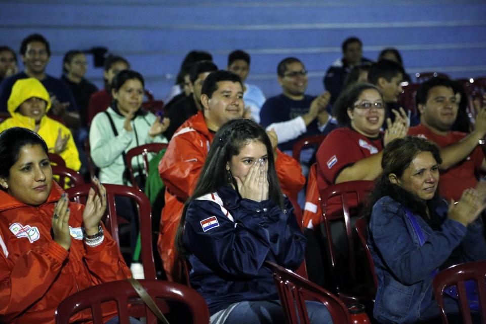 Paraguay's people react as they look at a TV screen showing the Vatican ceremony for a historic day of four popes, with Popes Francis and Benedict XVI honoring John XXIII and John Paul II by declaring them saints, at Nazareth church in Asuncion, Paraguay, Sunday, April 27, 2014. (AP Photo/Jorge Saenz)