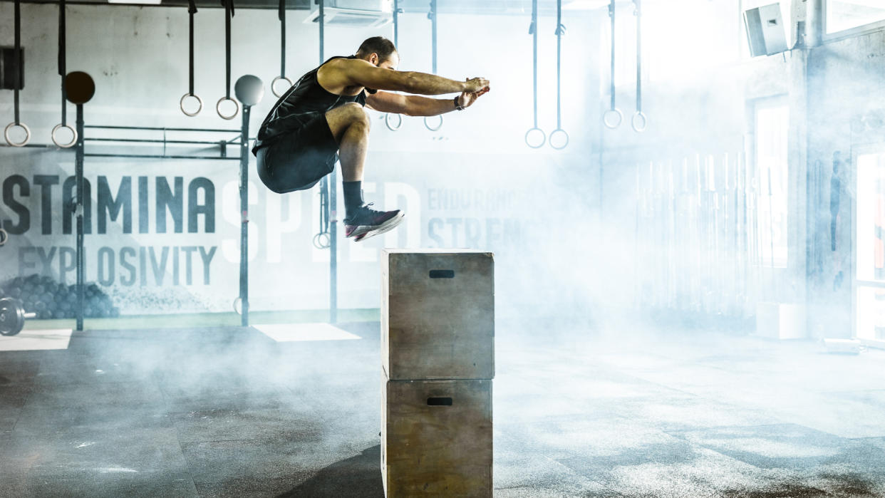 Athletic man jumping on a crate while having sports training in a gym.