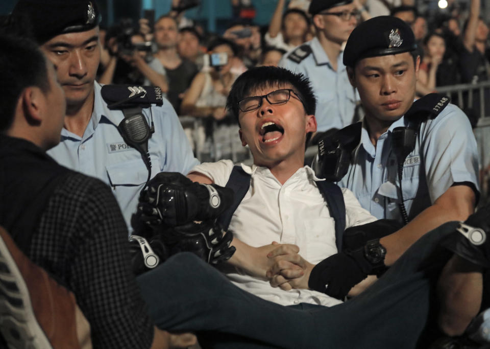 FILE - In this June 28, 2017, file photo, pro-democracy activist Joshua Wong is detained by police officers after he climb up to a giant flower statue bequeathed by Beijing in 1997 in Golden Bauhinia Square of Hong Kong. Overseas, Joshua Wong has emerged as a prominent face of Hong Kong's months-long protests for full democracy. At home, he is just another protester. (AP Photo/Vincent Yu, File)