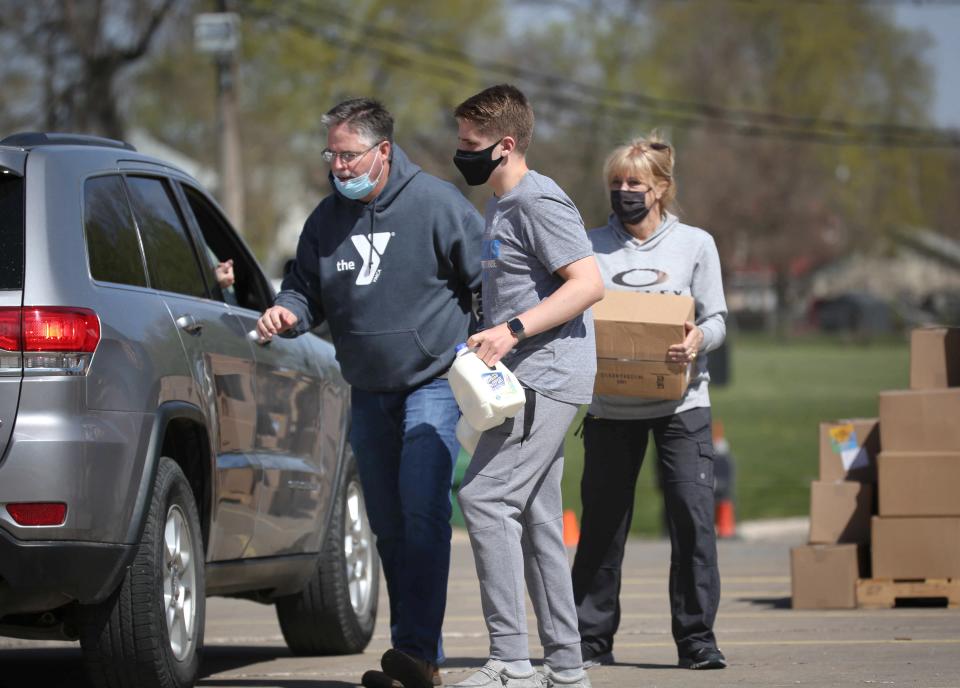 Volunteer Jack Gummert, 15, of Urbandale, carries two gallons of milk to a car while Kent Gummert and Melinda Hanrahan carry food boxes during the Farmers to Families food distribution event at the John R. Grubb YMCA in Des Moines on April 17.