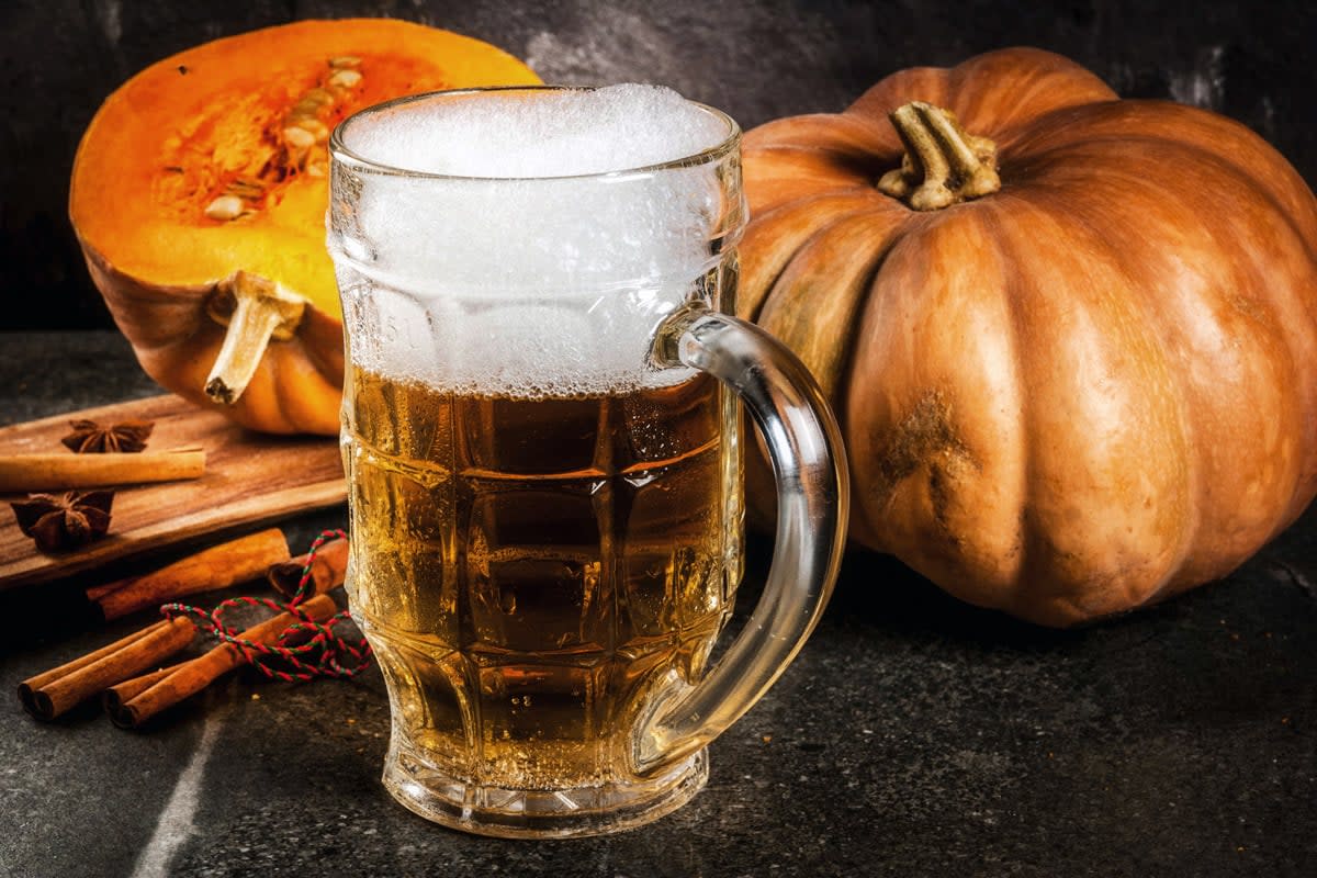 A pumpkin beer sits by two pumpkins.