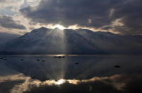 FILE- In this March 10, 2015 file photo, the sun peeks through a gap between clouds and a mountain as Kashmiri fishermen row their boats on their way home after working in Dal Lake in Srinagar, in Indian-controlled Kashmir. Kashmir’s pristine Alpine landscape, ski resorts, lake houseboat stays and uninterrupted acres of apple orchards have long made it a global tourist draw. (AP Photo/Dar Yasin, File)