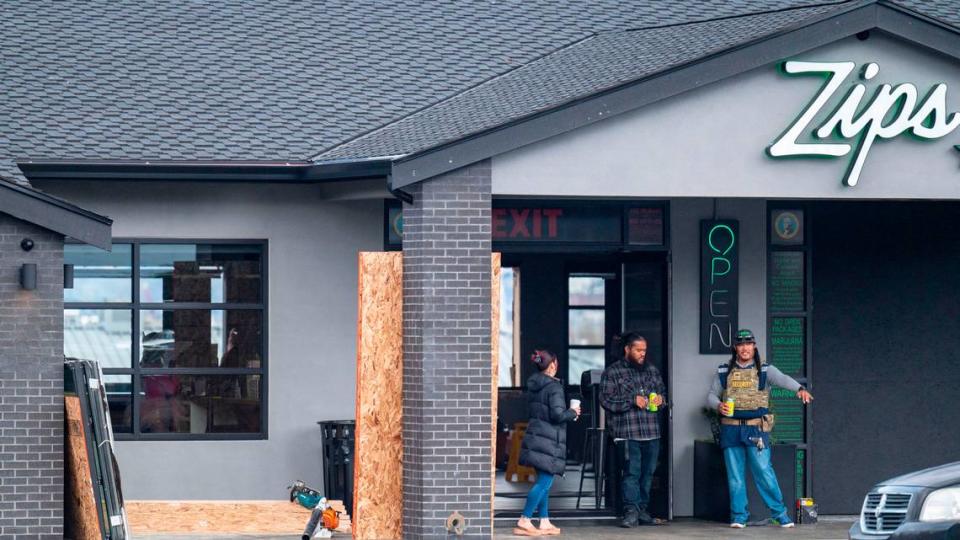 People stand outside the front entrance of Zips Cannabis on the 2600 block of Pacific Avenue in Tacoma, Wash., on Friday, Oct. 28, 2022. At 2:25 a.m. Friday morning, warning South Sound 911 that an armed robbery had occurred. It was reported by a security guard working for the cannabis shop. One of the vehicles involved in the robbery drove through the front of the store. The armed security guard exchanged gunfire with multiple suspects who fled on foot and in one of the vehicles.