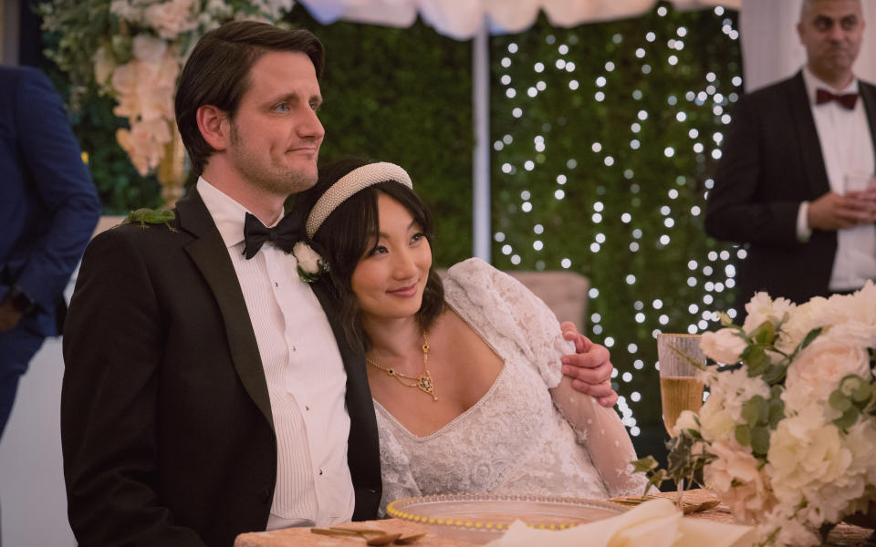 Edgar (Zach Woods) and Grace (Poppy Liu) in Episode 1 of the "Afterparty," seated together in an outdoor tent at their wedding. 