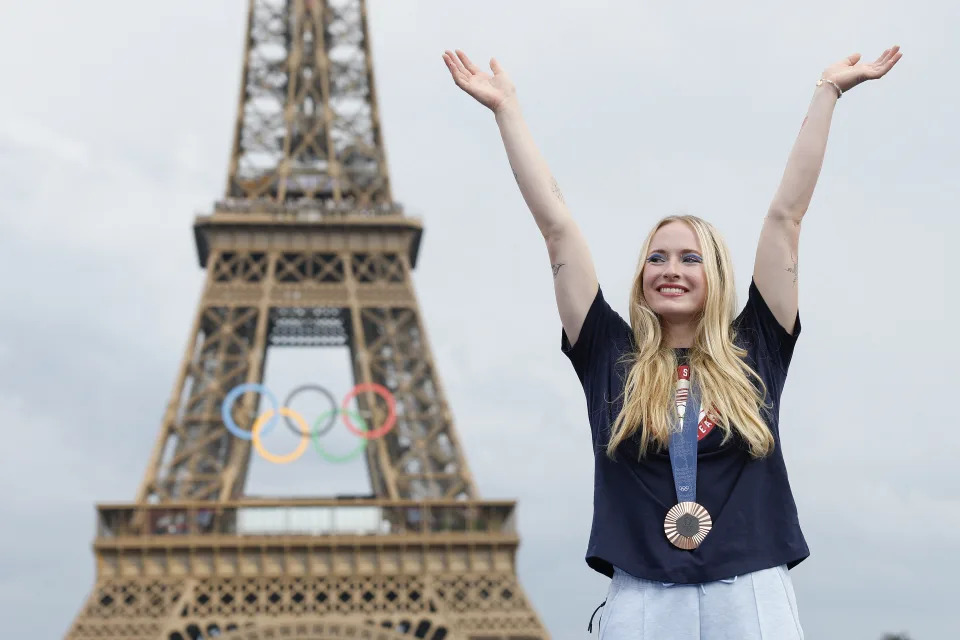 Evy Leibfarth, wearing a medal, raises her arms with the Eiffel Tower in the background.