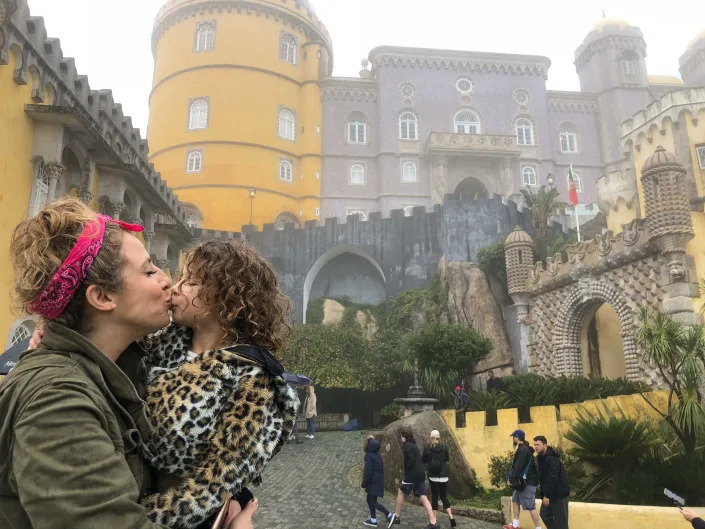 A woman kissing her child in front of colorful buildings.