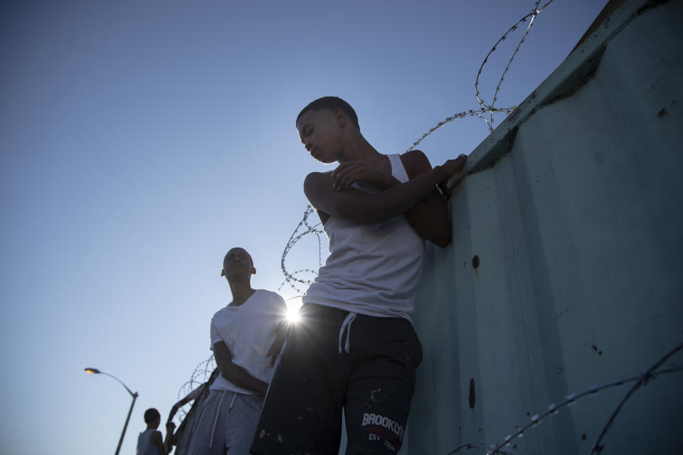 Protesters stand on a wall to catch a glimpse of South African president Cyril Ramaphosa visiting the family of 8-year-old Tazne Van Wyk in Cape Town, South Africa, on Feb. 25, 2020. The arrest of a 54-year-old sparked protests within the community calling for the death penalty. (AP Photo/Bram Janssen)