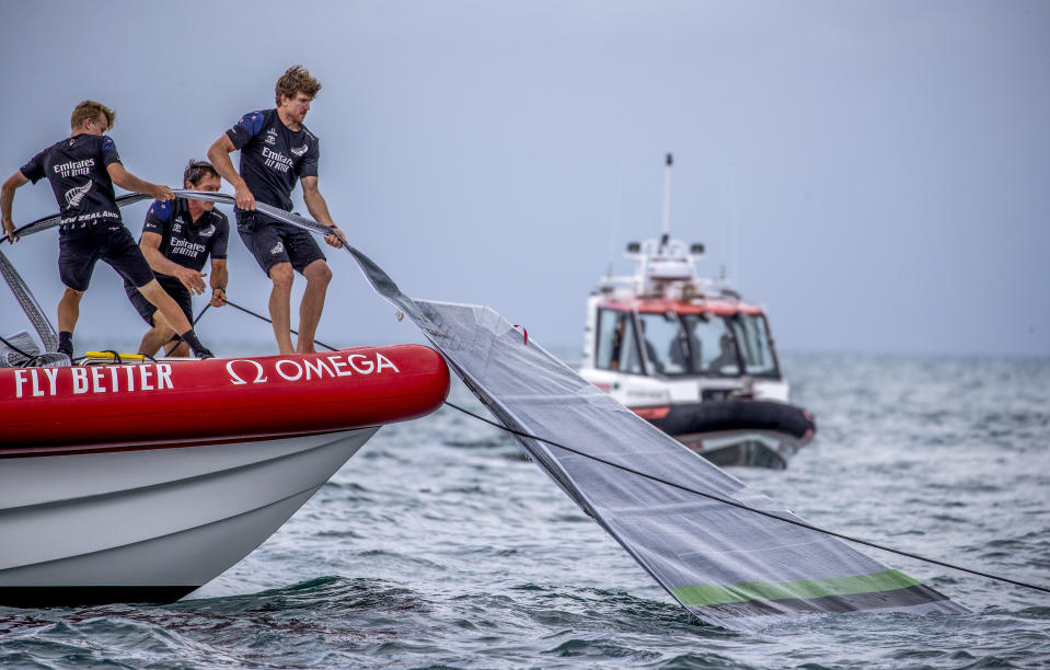 Team New Zealand crewmen grab the sail of United States' American Magic's boat, Patriot, after it capsized during its race against Italy's Luna Rossa on the third day of racing of the America's Cup challenger series on Auckland's Waitemate Harbour, New Zealand, Sunday, Jan. 17, 2021. (Michael Craig/NZ Herald via AP)