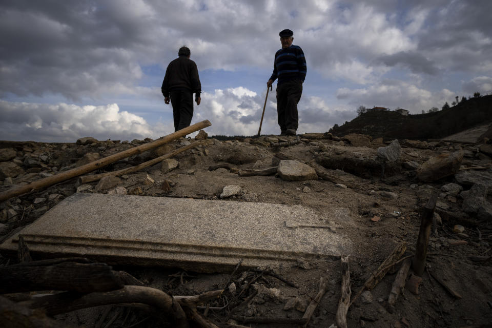 Julio Penin, 78, looks at a grave as they visit the old village of Aceredo emerged due to drought at the Lindoso reservoir, in northwestern Spain, Friday, Feb. 11, 2022. Roofs emerging from the waters have become a common scene every summer at the Lindoso reservoir, in northwestern Spain. In especially dry years, parts of the old village of Aceredo, submerged three decades ago when a hydropower dam flooded the valley, would appear. But never before had the skeleton of the village emerged in its entirety, in the middle of the usually wet winter season. (AP Photo/Emilio Morenatti)