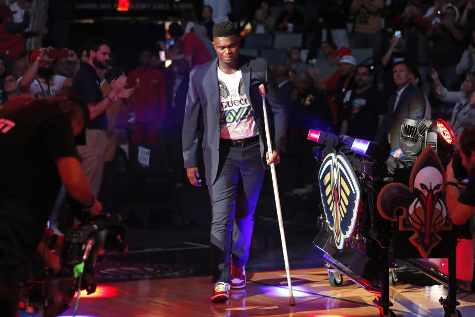 New Orleans Pelicans forward Zion Williamson walk onto the court with a crutch as he is introduced before an NBA basketball home-opener game against the Dallas Mavericks in New Orleans, Friday, Oct. 25, 2019. (AP Photo/Gerald Herbert)