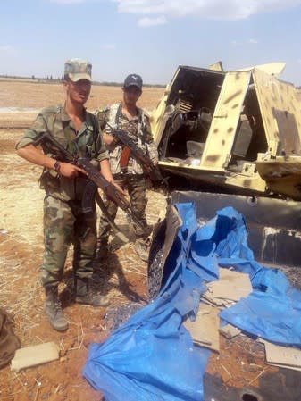 Syrian army soldiers hold their weapons as they stand next to a damaged military tank in Idlib countryside